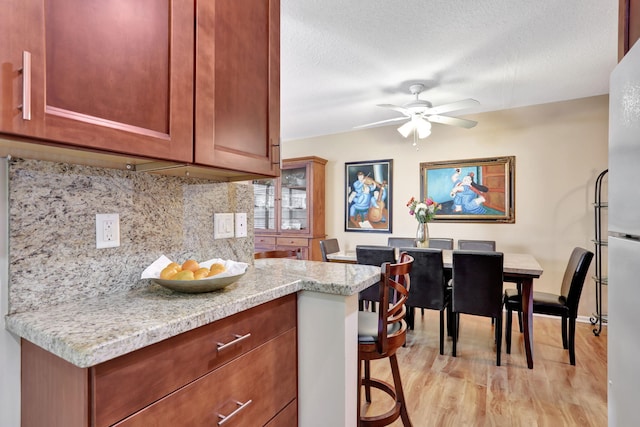 kitchen featuring decorative backsplash, ceiling fan, light stone countertops, a textured ceiling, and light hardwood / wood-style flooring