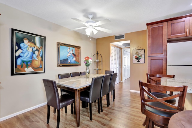 dining space with ceiling fan, a textured ceiling, and light hardwood / wood-style floors