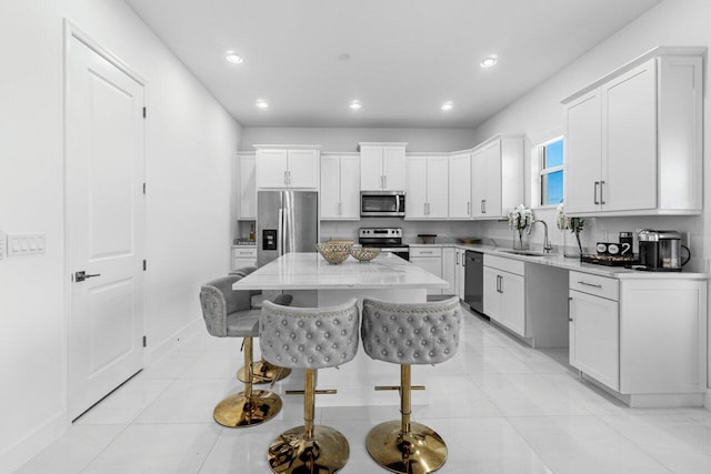 kitchen featuring a breakfast bar, a kitchen island, white cabinetry, appliances with stainless steel finishes, and sink