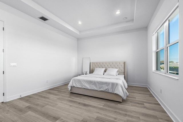 bedroom with light hardwood / wood-style floors and a tray ceiling