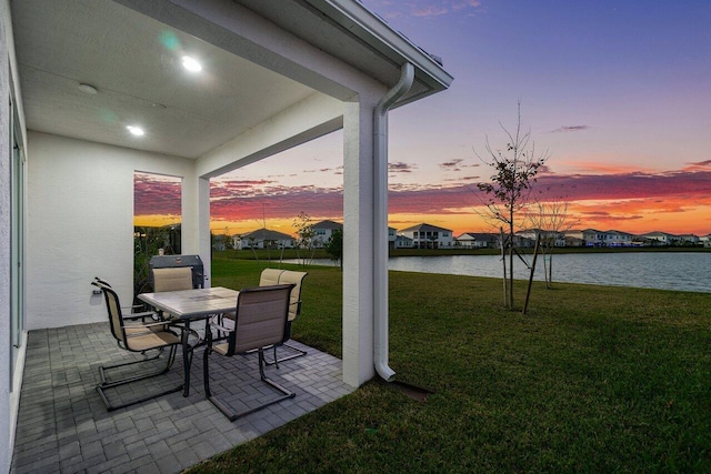 patio terrace at dusk featuring a yard and a water view