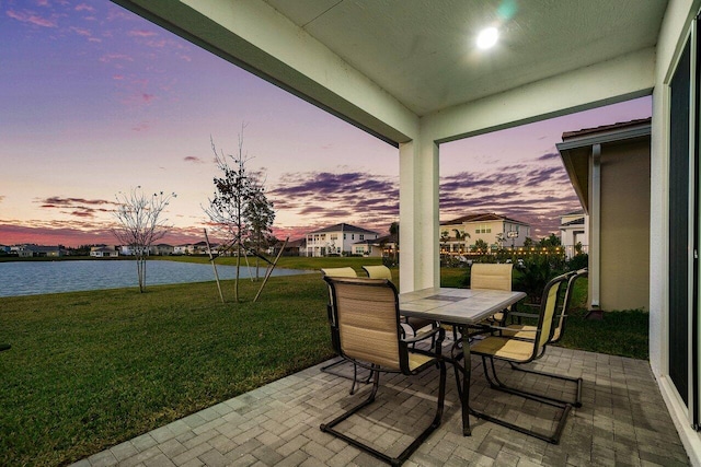 patio terrace at dusk featuring a lawn and a water view