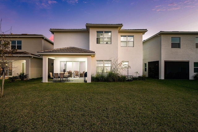 back house at dusk with a yard and a patio area