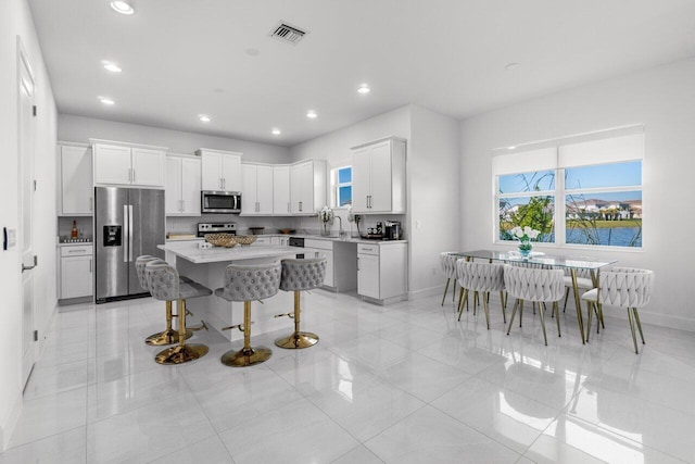 kitchen featuring a center island, a kitchen bar, white cabinets, appliances with stainless steel finishes, and sink