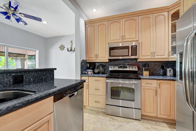 kitchen with appliances with stainless steel finishes, light tile patterned floors, ceiling fan, dark stone counters, and light brown cabinetry