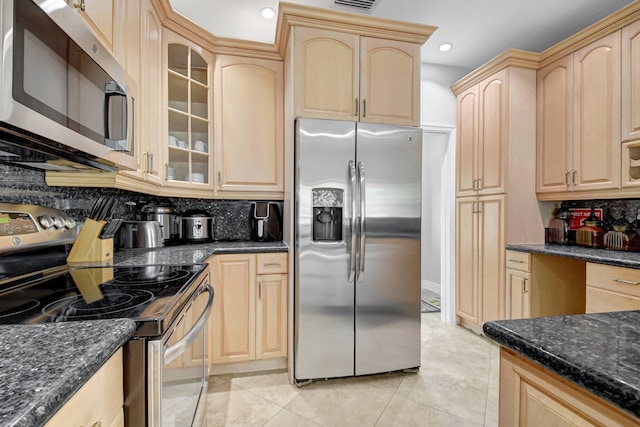 kitchen with light tile patterned floors, tasteful backsplash, appliances with stainless steel finishes, dark stone countertops, and light brown cabinets