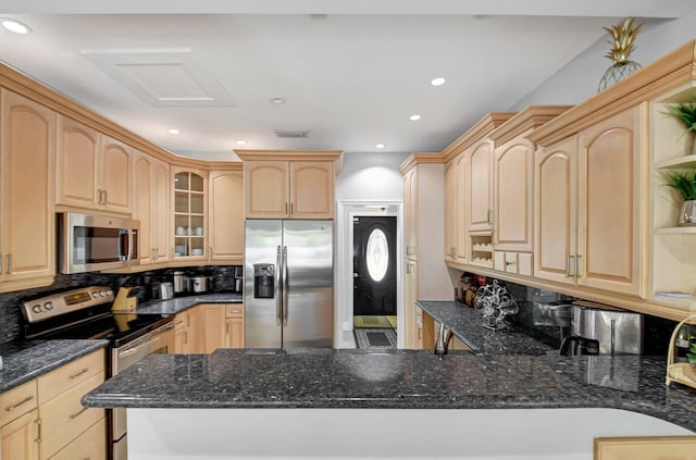 kitchen with dark stone counters, stainless steel appliances, light brown cabinetry, and kitchen peninsula