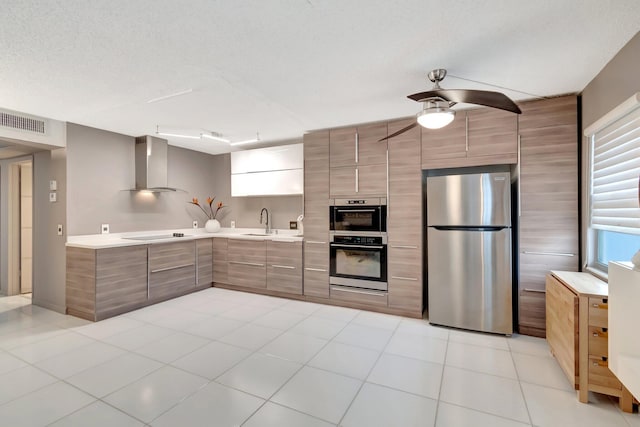 kitchen with stainless steel appliances, ceiling fan, wall chimney exhaust hood, sink, and light tile patterned flooring