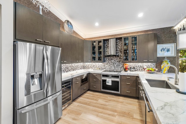 kitchen featuring beverage cooler, appliances with stainless steel finishes, wall chimney exhaust hood, sink, and dark brown cabinets