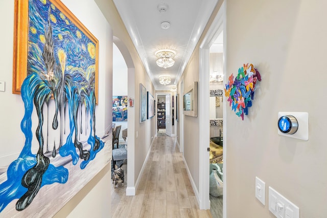 hallway with crown molding, a chandelier, and light wood-type flooring