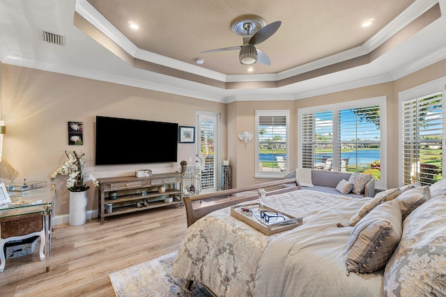 bedroom with ceiling fan, multiple windows, light hardwood / wood-style flooring, and a raised ceiling