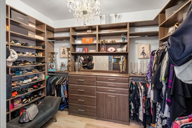 spacious closet with light hardwood / wood-style flooring and an inviting chandelier