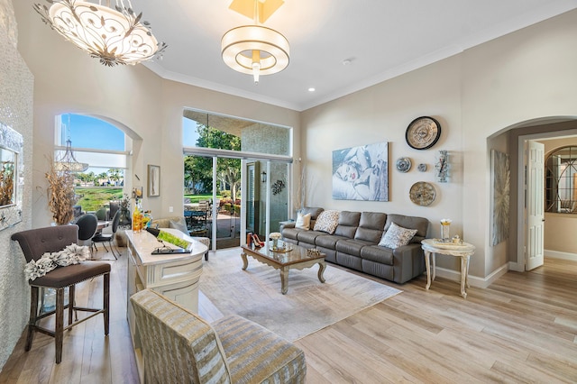 living room featuring crown molding, an inviting chandelier, light wood-type flooring, and a high ceiling