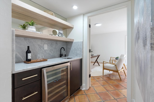 bar featuring beverage cooler, light tile patterned floors, dark brown cabinetry, sink, and backsplash