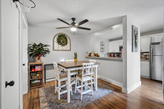 dining room with a textured ceiling, rail lighting, ceiling fan, and dark hardwood / wood-style floors