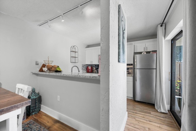 kitchen featuring track lighting, light stone countertops, a textured ceiling, stainless steel fridge, and white cabinets