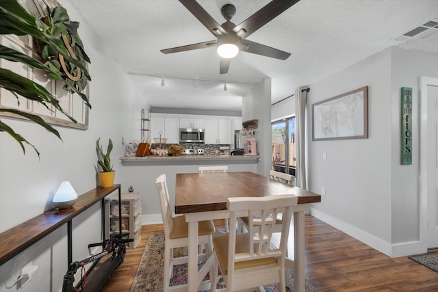 dining room featuring dark wood-type flooring, track lighting, ceiling fan, and a textured ceiling