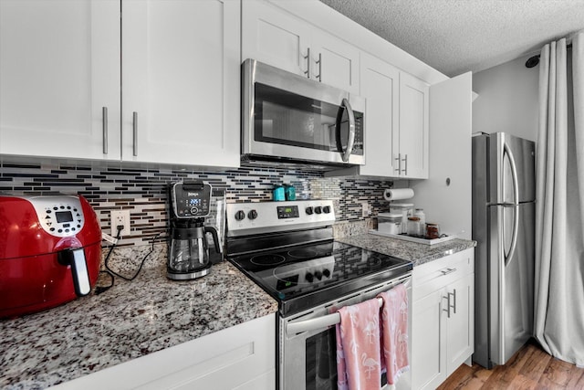 kitchen with stainless steel appliances, white cabinetry, and light stone counters