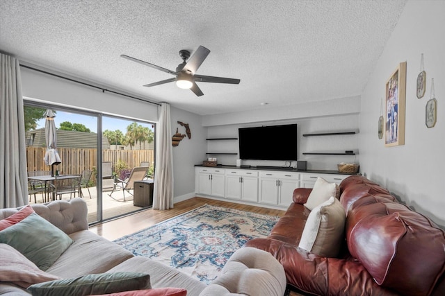 living room featuring light wood-type flooring, ceiling fan, and a textured ceiling