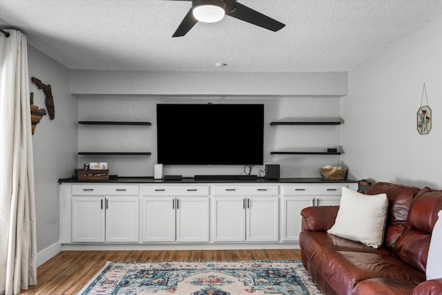 living room with a textured ceiling, ceiling fan, and light wood-type flooring