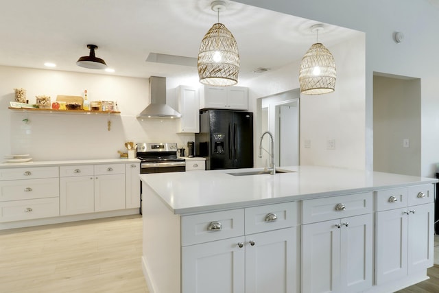 kitchen with electric stove, light countertops, black fridge, wall chimney range hood, and a sink