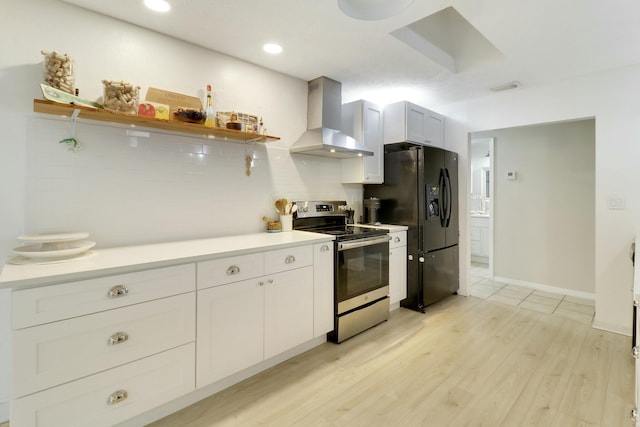 kitchen with light wood finished floors, decorative backsplash, wall chimney exhaust hood, stainless steel range with electric stovetop, and black fridge