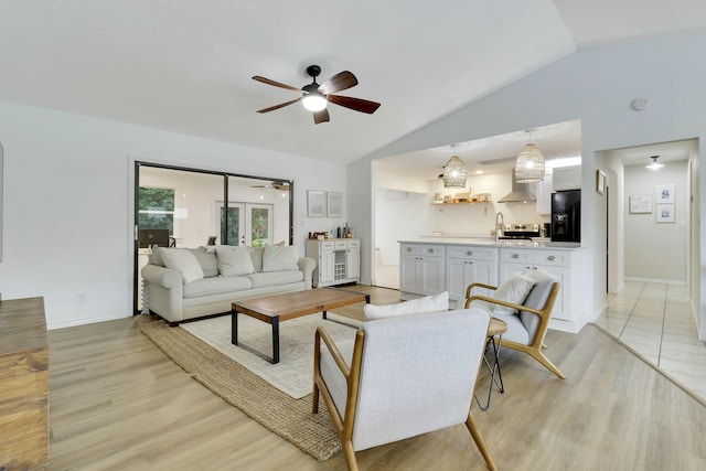 living room with lofted ceiling, ceiling fan, light wood-type flooring, and baseboards