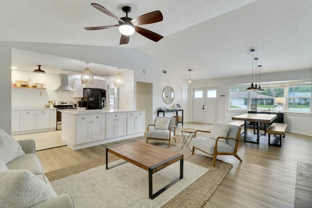 living area featuring lofted ceiling, a ceiling fan, a textured ceiling, light wood-type flooring, and baseboards