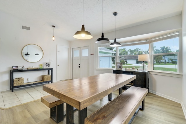 dining room with lofted ceiling, visible vents, light wood-style flooring, a textured ceiling, and baseboards