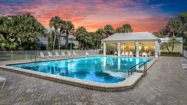 pool at dusk with a patio area and ceiling fan