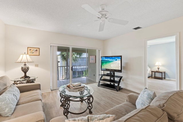 living room with a textured ceiling, ceiling fan, and light hardwood / wood-style floors