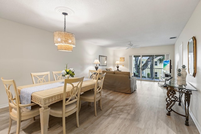 dining area with ceiling fan with notable chandelier, a textured ceiling, and light hardwood / wood-style flooring