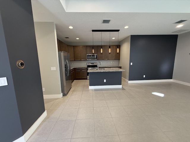 kitchen with stainless steel appliances, light tile patterned floors, an island with sink, hanging light fixtures, and light stone countertops