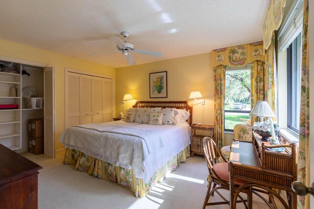 carpeted bedroom with multiple closets, ceiling fan, and a textured ceiling