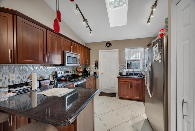 kitchen featuring sink, light tile patterned floors, appliances with stainless steel finishes, dark stone countertops, and lofted ceiling with skylight