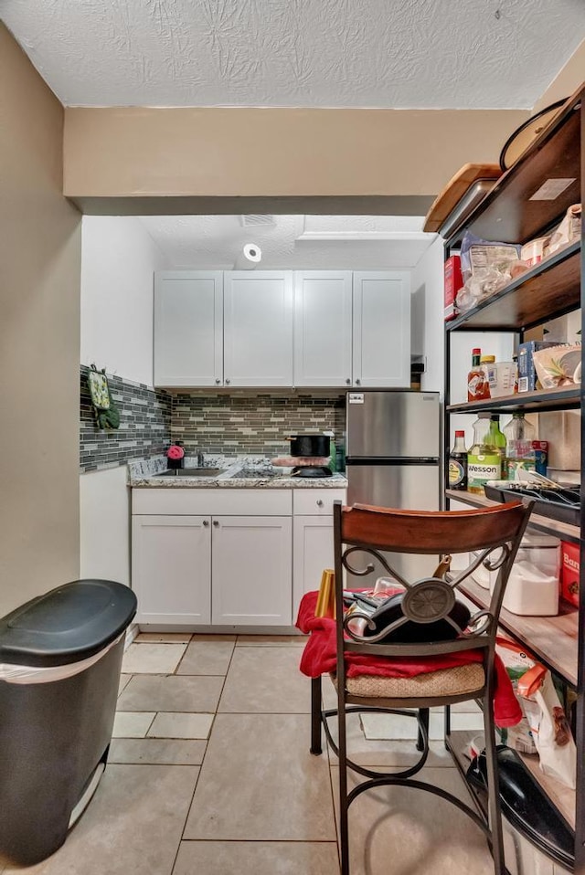 kitchen featuring tasteful backsplash, white cabinets, stainless steel fridge, light tile patterned floors, and light stone countertops