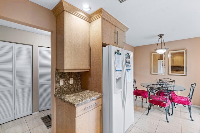 kitchen with white refrigerator with ice dispenser, dark stone countertops, hanging light fixtures, light tile patterned floors, and decorative backsplash