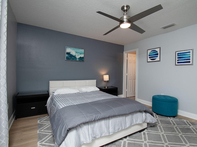 bedroom featuring visible vents, ceiling fan, a textured ceiling, wood finished floors, and baseboards