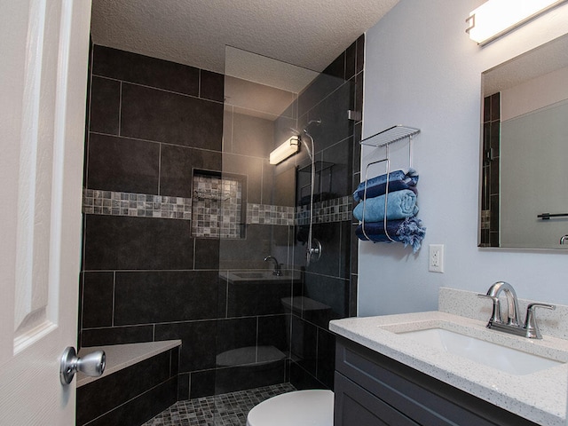 bathroom with toilet, a textured ceiling, tiled shower, and vanity