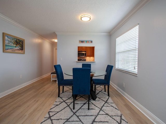 dining room featuring a textured ceiling, ornamental molding, light wood-style flooring, and baseboards