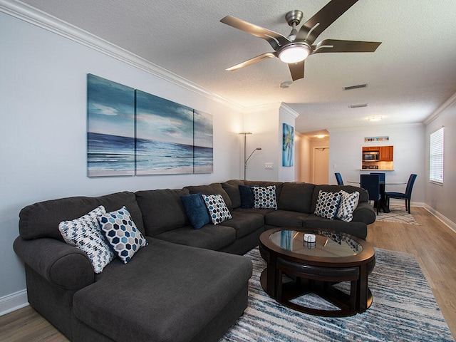 living room with a textured ceiling, visible vents, crown molding, and wood finished floors