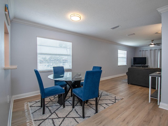 dining room with crown molding, a textured ceiling, visible vents, and wood finished floors