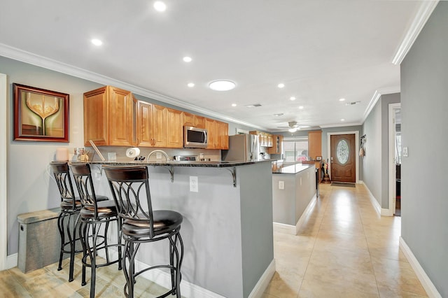 kitchen with kitchen peninsula, ceiling fan, appliances with stainless steel finishes, a kitchen breakfast bar, and crown molding