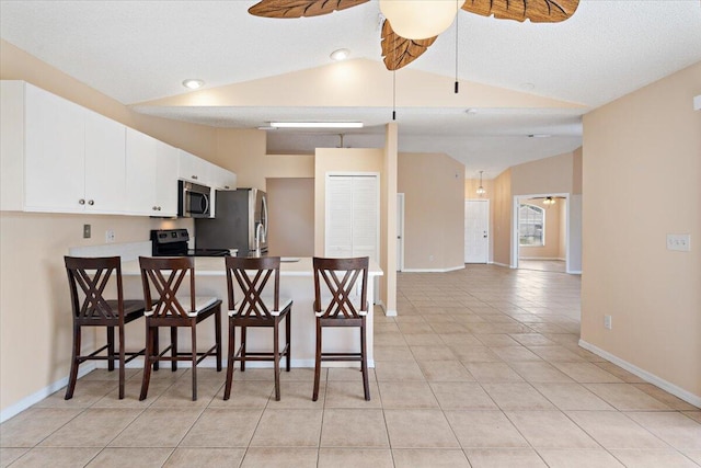 kitchen with lofted ceiling, a kitchen bar, appliances with stainless steel finishes, kitchen peninsula, and white cabinets