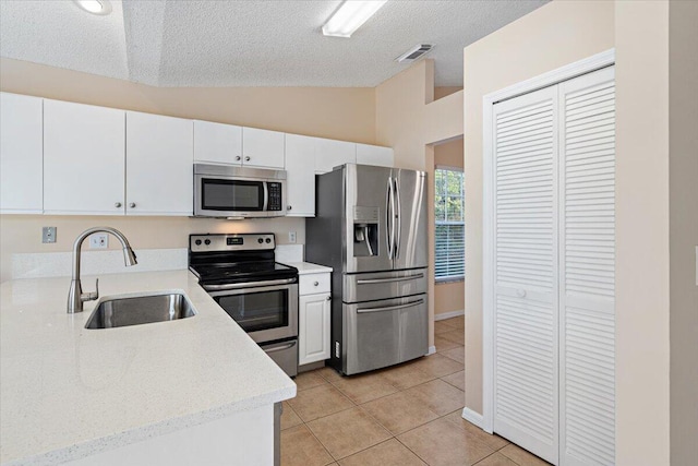 kitchen with sink, vaulted ceiling, light tile patterned floors, appliances with stainless steel finishes, and white cabinets