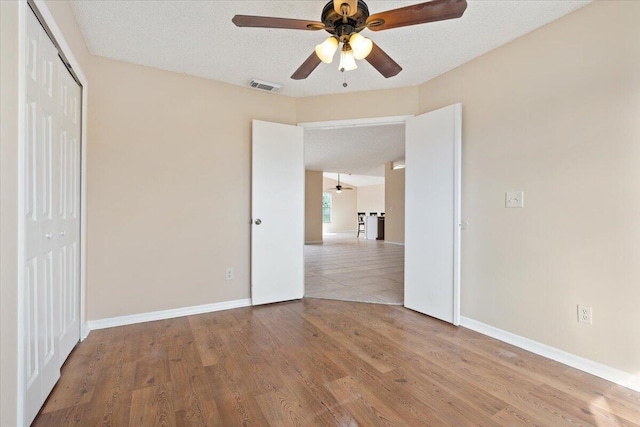 unfurnished bedroom with ceiling fan, a textured ceiling, a closet, and light wood-type flooring