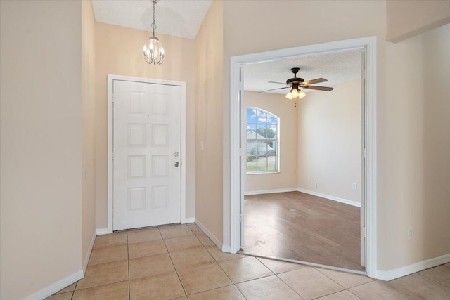 foyer with ceiling fan with notable chandelier, light tile patterned floors, and a textured ceiling