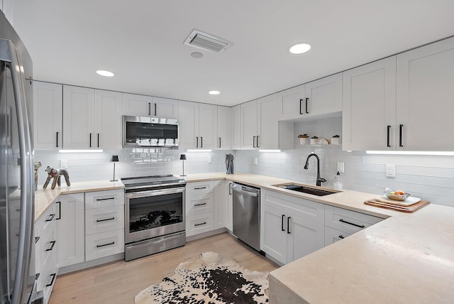 kitchen with appliances with stainless steel finishes, light hardwood / wood-style floors, white cabinets, and sink