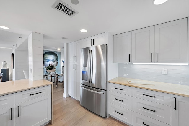 kitchen featuring stainless steel refrigerator with ice dispenser, white cabinetry, decorative backsplash, and light hardwood / wood-style floors