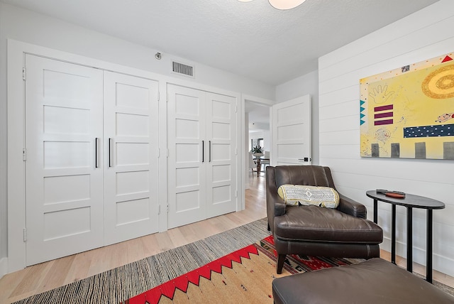 living area with hardwood / wood-style flooring, a textured ceiling, and wooden walls